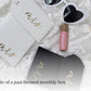 A styled flat lay of a honeymoon gift box contents showing a white leather wallet/card holder with gold script reading 'mrs.', white heart-shaped sunglasses, a pink lip balm tube, and black Mr gift tags on a white textured fabric background.