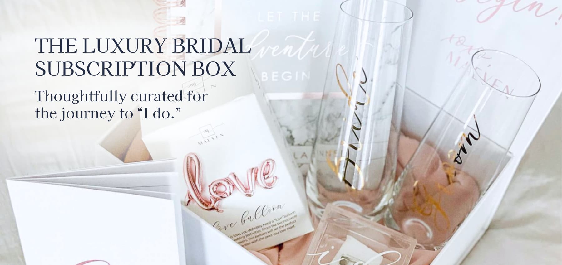 A luxury bridal subscription box containing bride and groom champagne flutes, a ring box, a custom wedding planner, vow books, a love balloon
