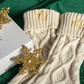 Ivory knitted christmas stockings with 'Mr' and 'Mrs' embroidery, gold snowflake decorations, and Maeven box on green fabric.